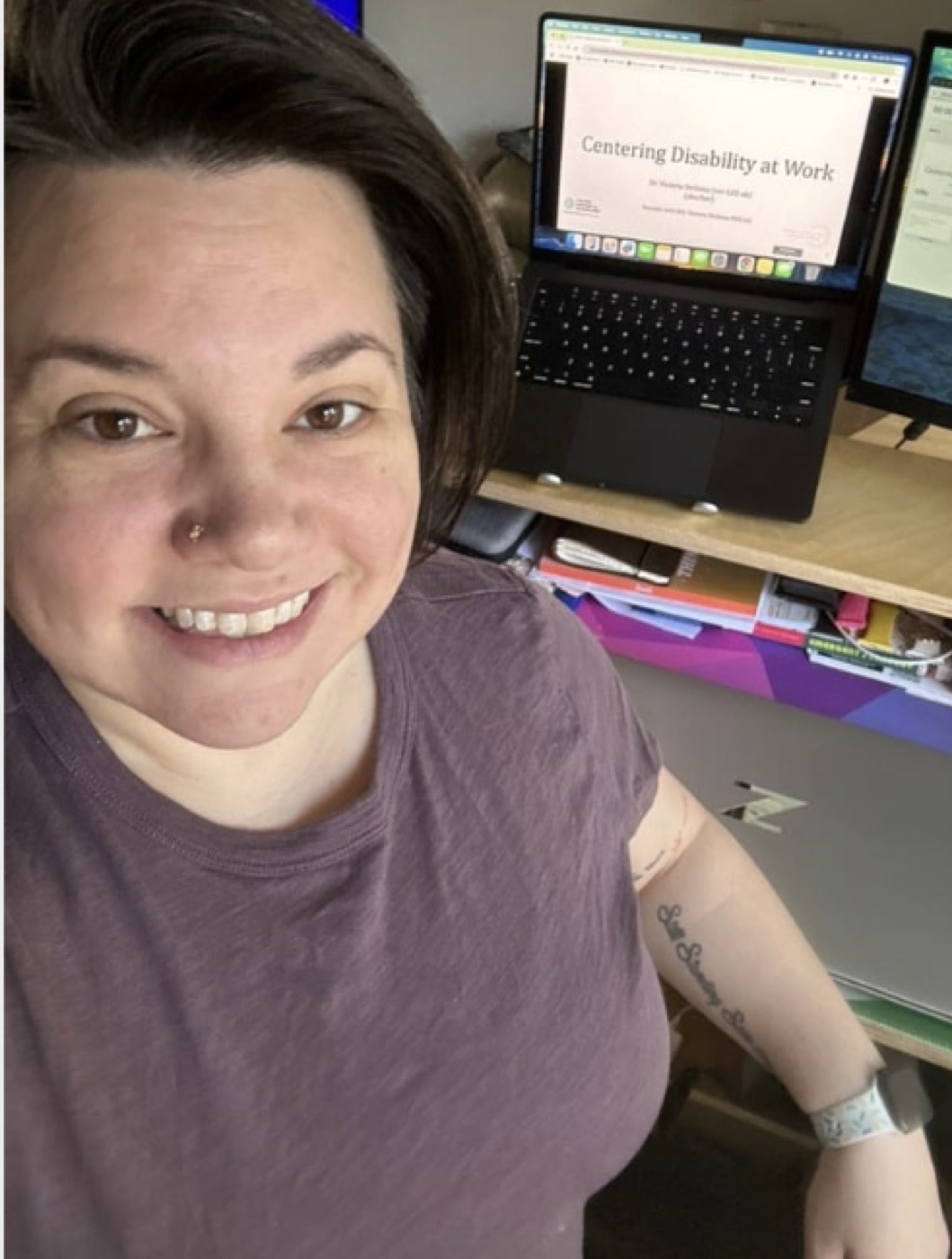 Dr. Victoria Verlezza at her desk, with her talk Centering Disability at Work on the laptop behind her